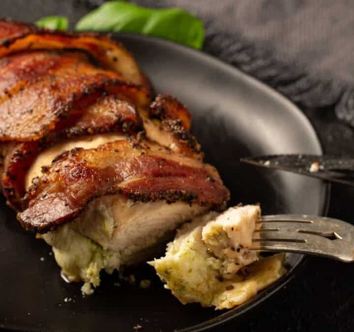 A bacon wrapped chicken breast on a plate with a knife and fork.