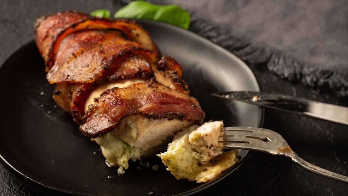 A bacon wrapped chicken breast on a plate with a knife and fork.