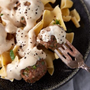 A fork piercing a baked meatball covered in gravy.