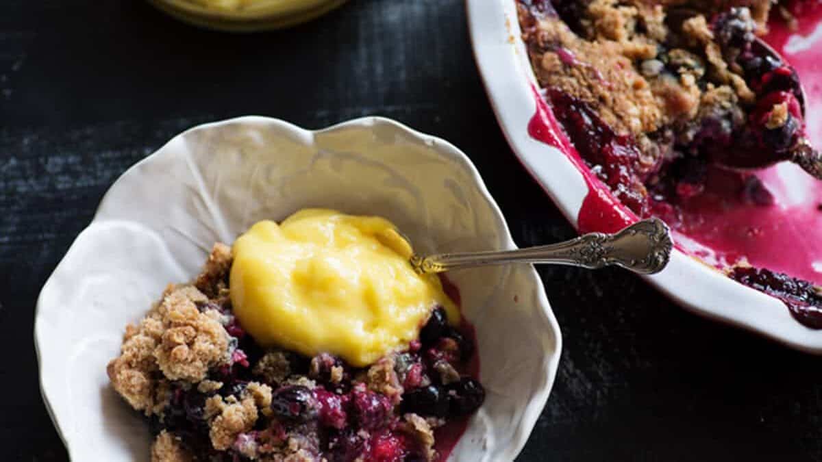 A bowl of blueberry crisp next to a baking dish.