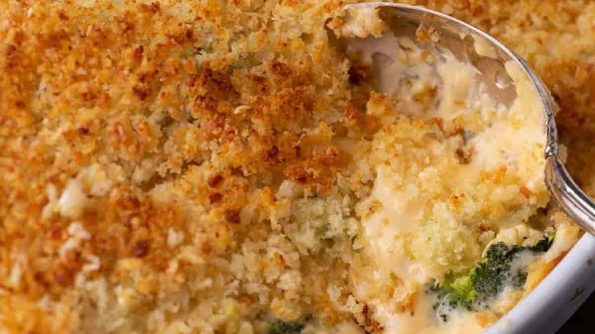 A spoon full of cheesy broccoli casserole in a baking dish.