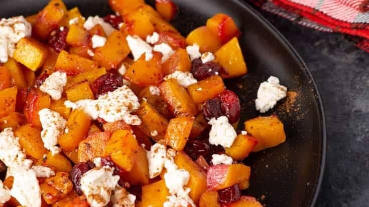 A black platter with roasted butternut squash with cranberries and feta