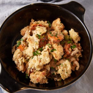 A black bowl filled with savory stuffing. The dish includes chunks of seasoned bread, pieces of tender vegetables like carrots and celery, and garnished with fresh herbs. The stuffing has a rich, textured appearance, typical of a hearty, homecooked meal.