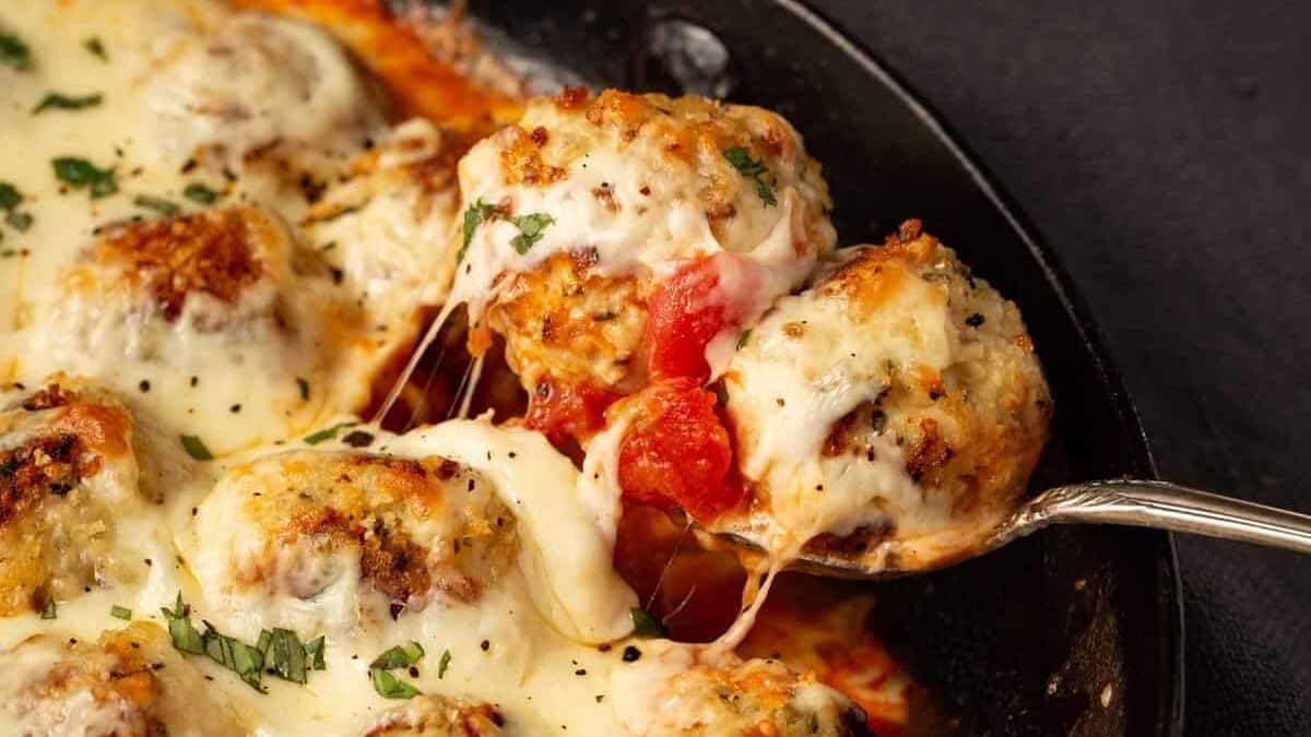 A skillet of Chicken parmesan meatballs with a serving spoon.