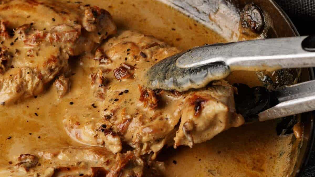 A chicken breast being removed from a skillet