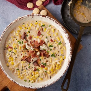 A bowl of soup with corn and crab next to a ladle.