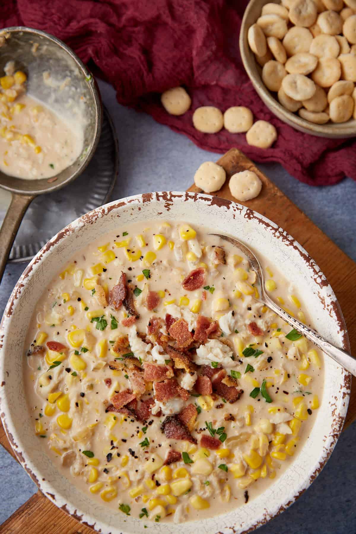 A bowl of corn and crab bisque next to a ladel and crackers.
