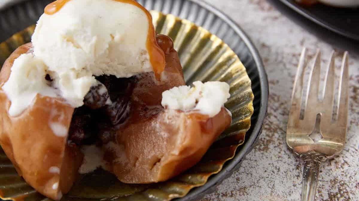 An individual baked apple on a plate next to caramel sauce.