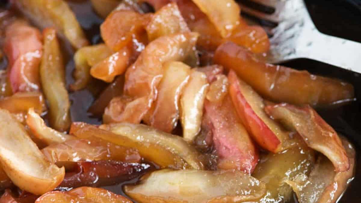 An iron skillet with fried apples and a spoon.