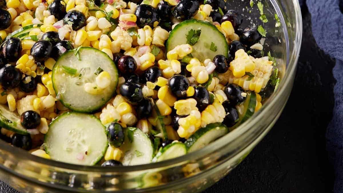 A clear glass bowl of corn salad with blueberries.