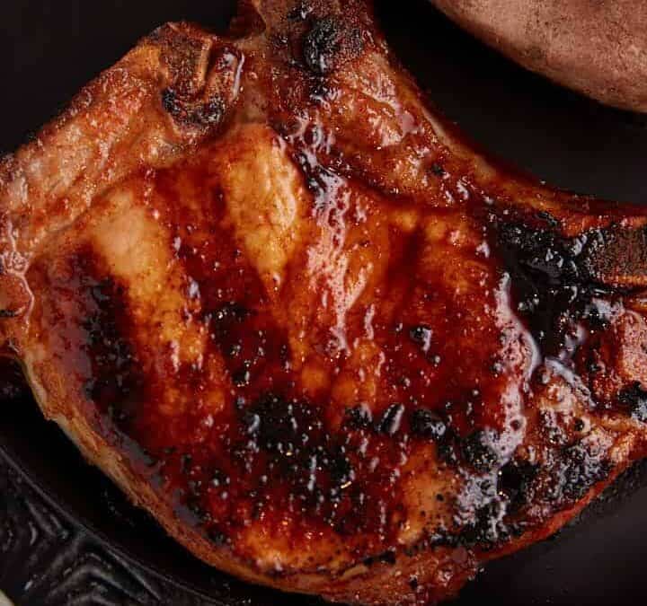 A grilled pork chop next to a sweet potato on a plate.
