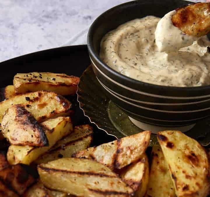 Someone dipping a potato into a bowl of sauce.