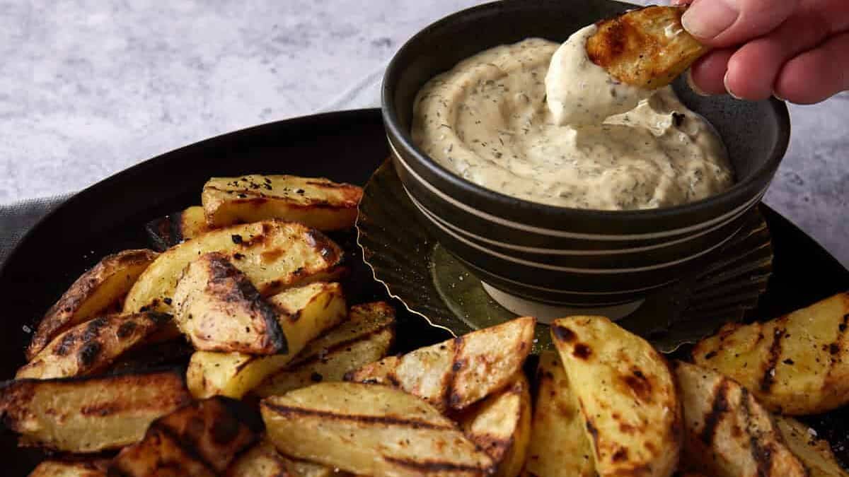 Someone dipping a potato into a bowl of sauce.
