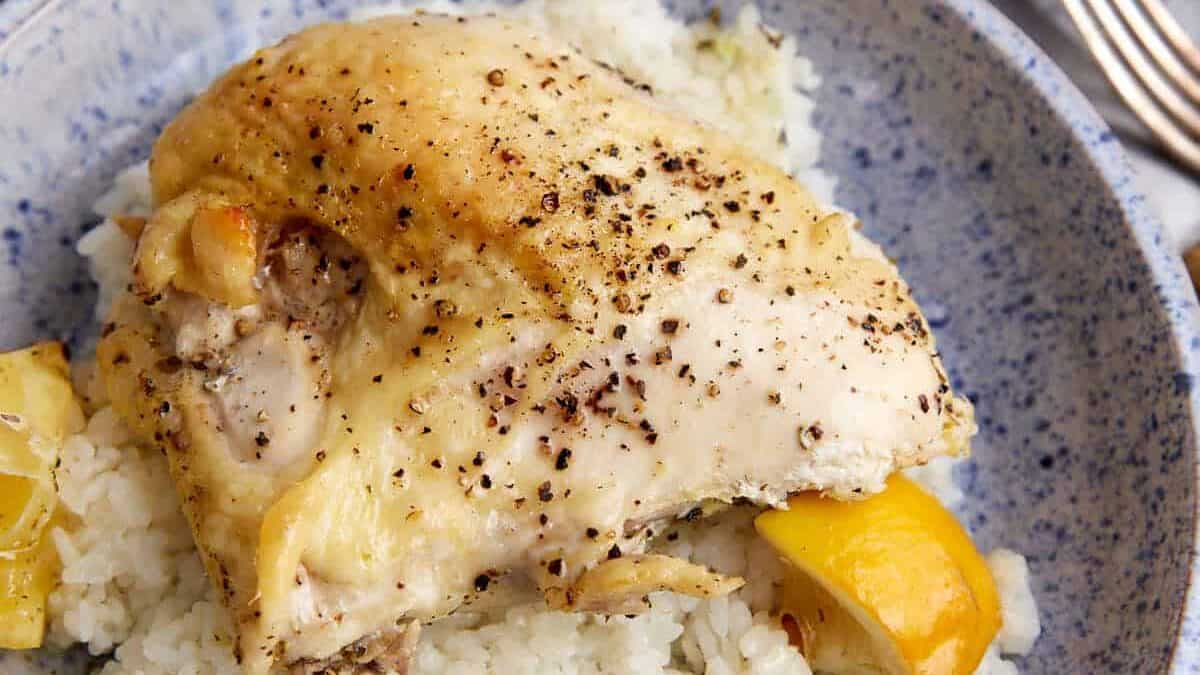 A baked chicken breast on a bed of rice with lemon wedges.
