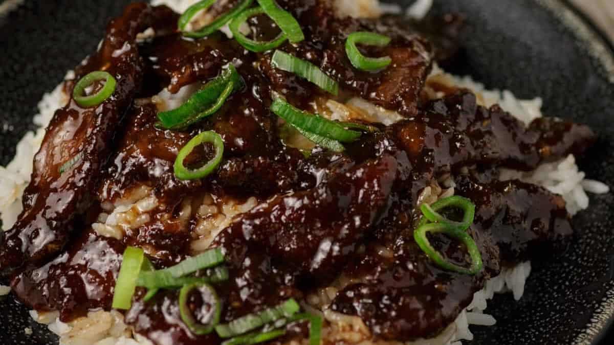 A black platter of rice topped with Mongolian beef stir fry.