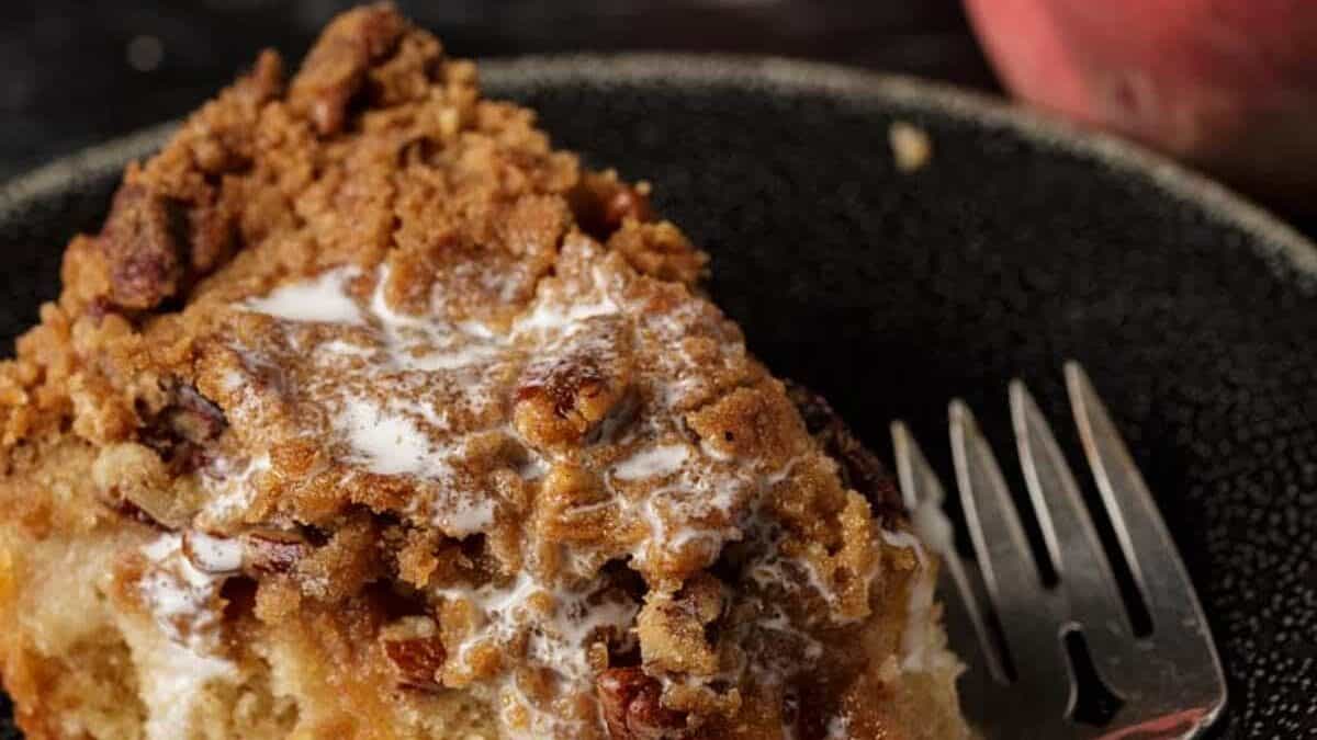 Cream dripping off a slice of coffee cake with peaches.