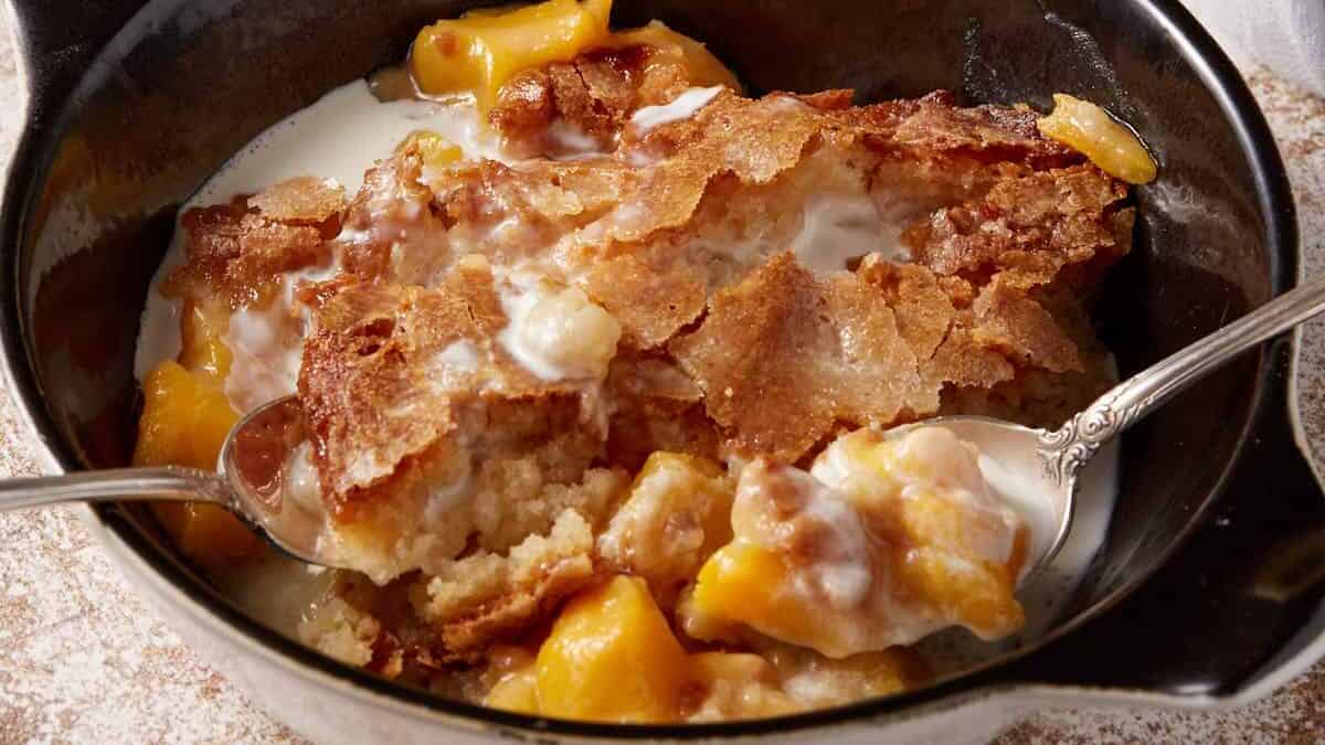 A black bowl of peach cobbler next to a cup of coffee.