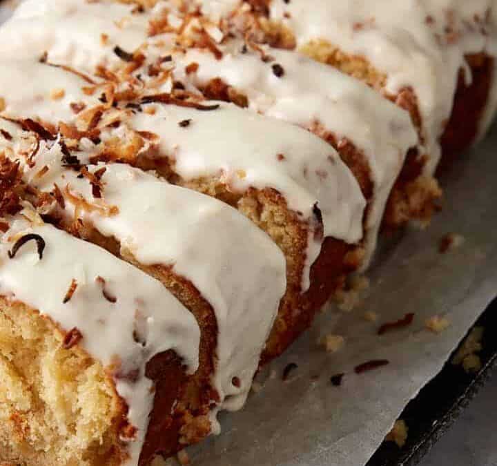 A loaf of coconut bread with frosting and coconut flakes.