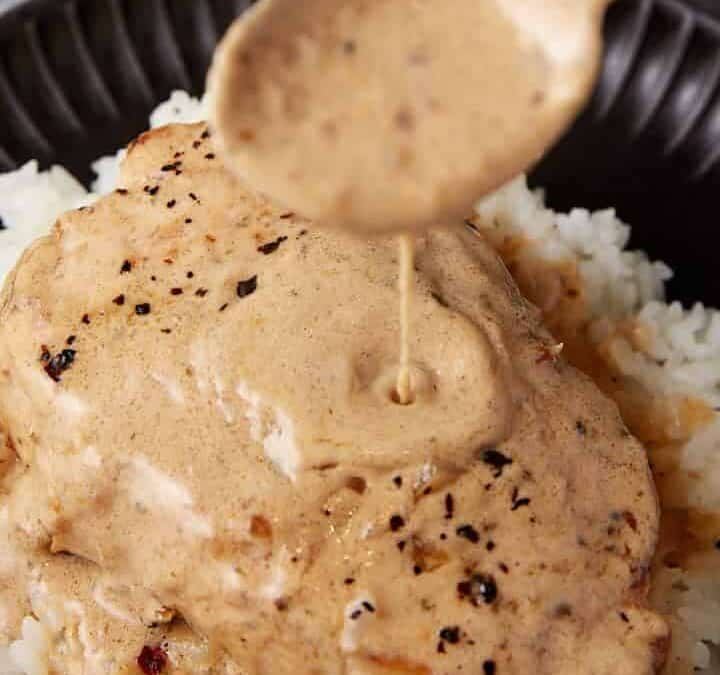 A spoon pouring gravy over pork chops.