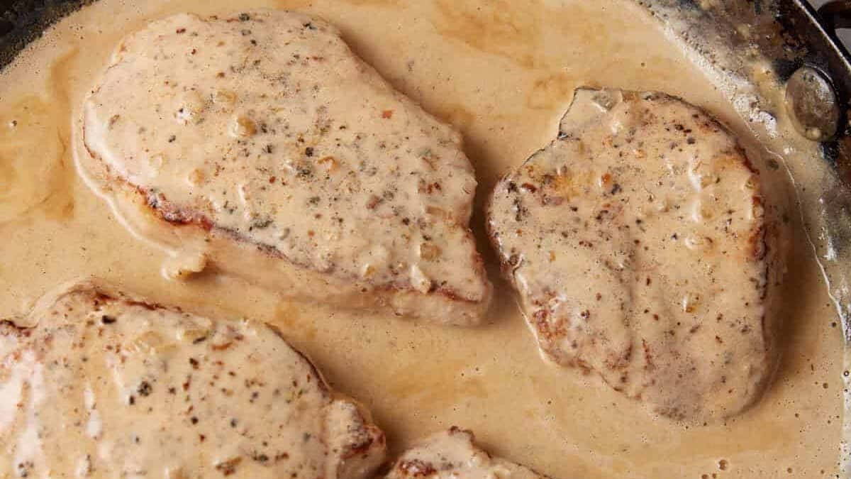 Pork chops simmering in a skillet with gravy.