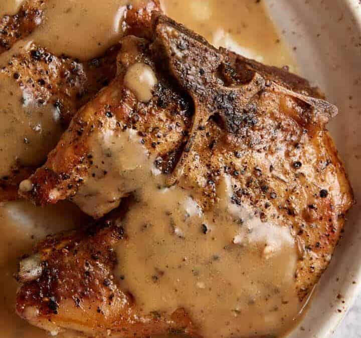 Pork chops on a plate covered with ranch gravy.