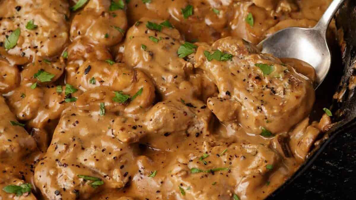 A serving spoon in a skillet of pork marsala medallions