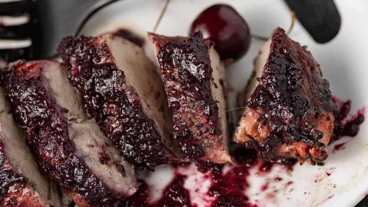 A sliced pork tenderloin on a platter with cherry sauce around it.