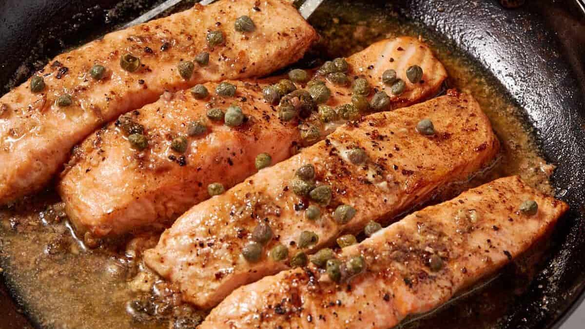 A skillet of salmon fillets with a spatula and a lemon.