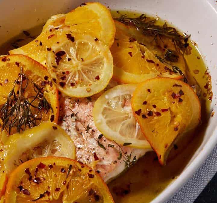 Baked salmon in a dish next to a bowl of lemon slices.