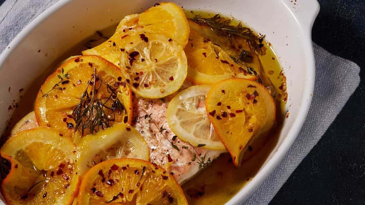 Baked salmon in a dish next to a bowl of lemon slices.