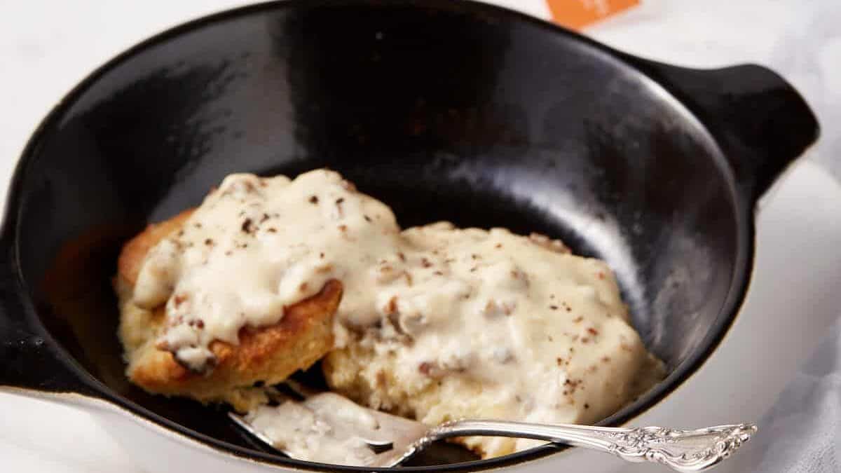 Sausage gravy poured over biscuits in a black casserole dish.