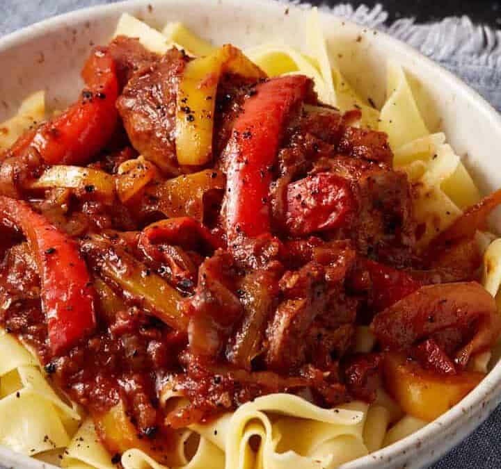 A bowl of sausage and pepper pasta next to crusty bread.