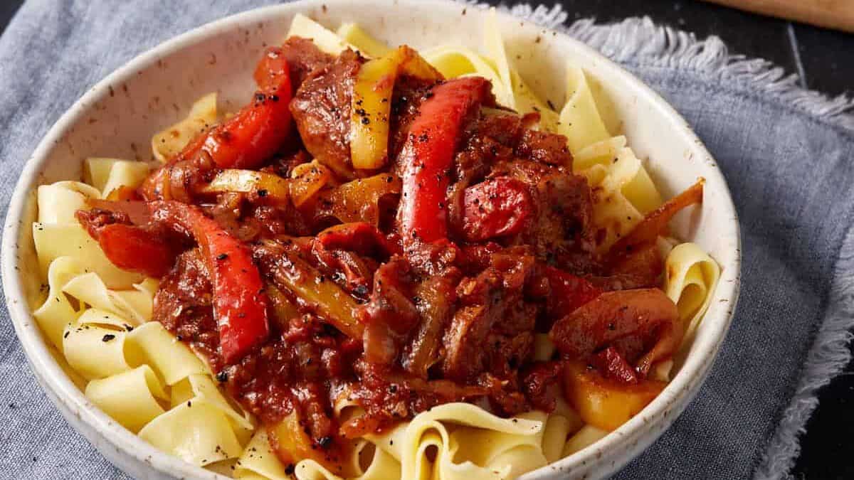 A bowl of sausage and pepper pasta next to crusty bread.