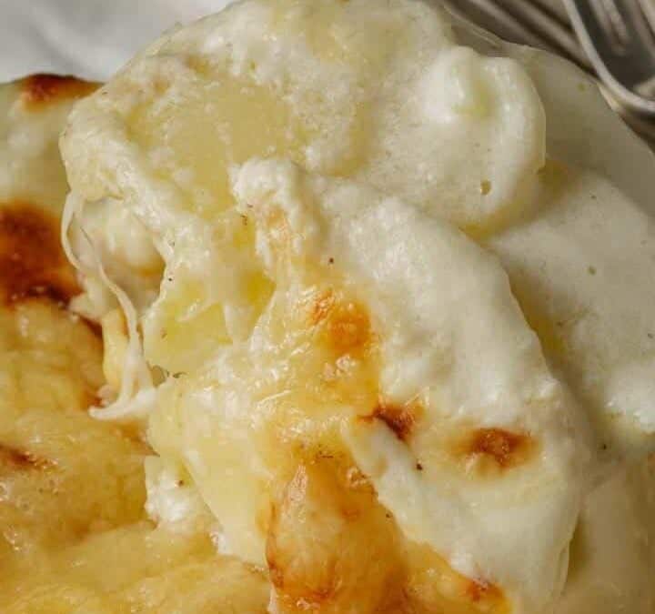 A spoon full of au gratin potatoes with cheese.