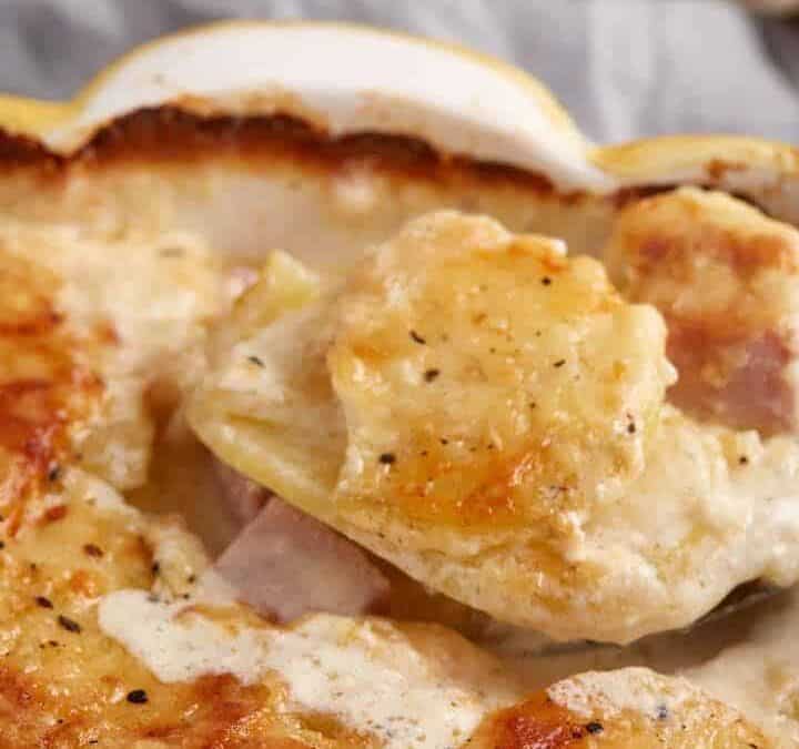 A serving spoon removing some potato and ham casserole.