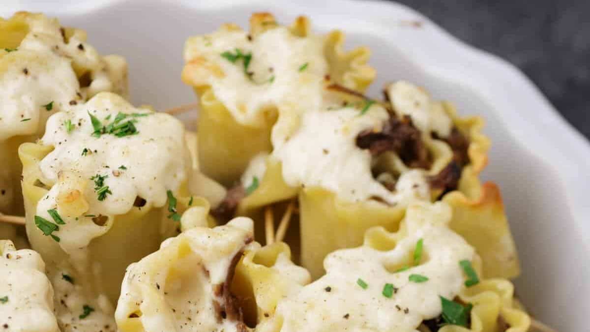 A casserole dish full of lasagna rolls covered in a cheese sauce.
