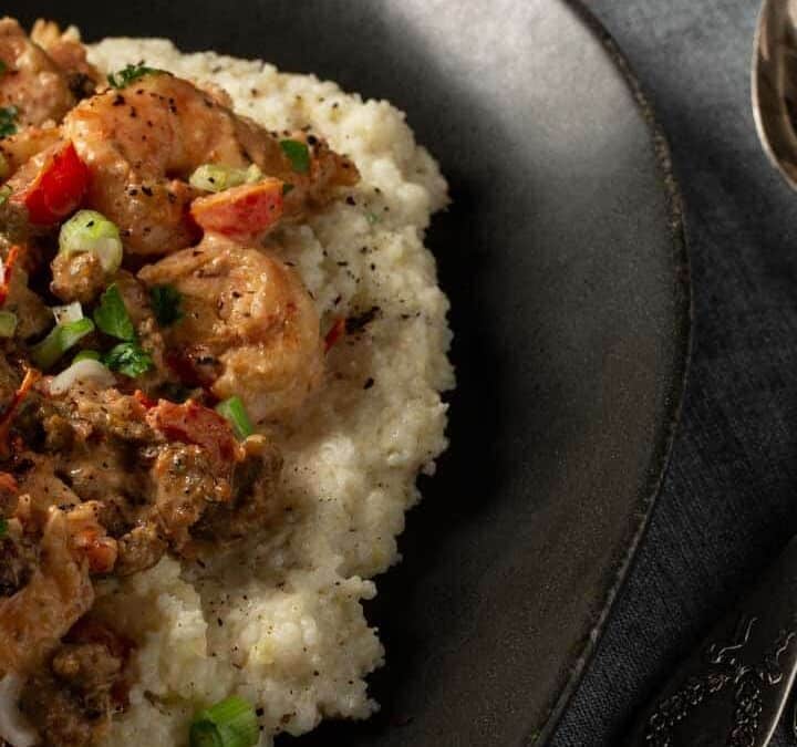 A platter of shrimp and grits with two glasses of wine.