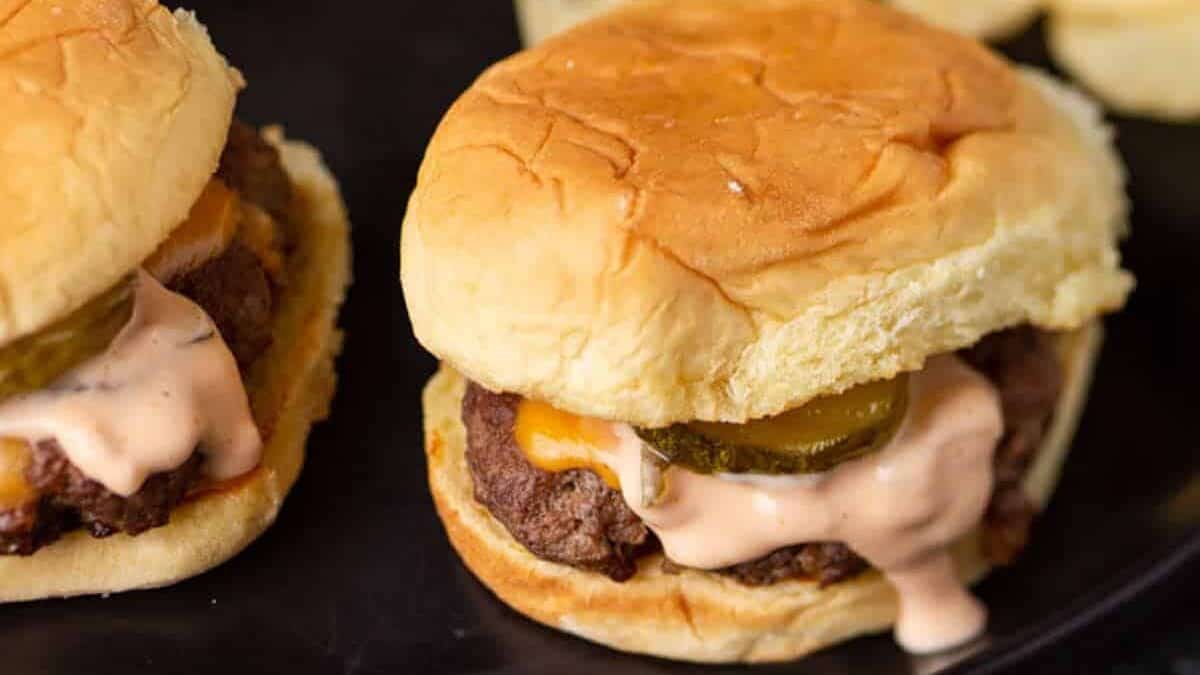 Two Smash burgers in buns with sauce.