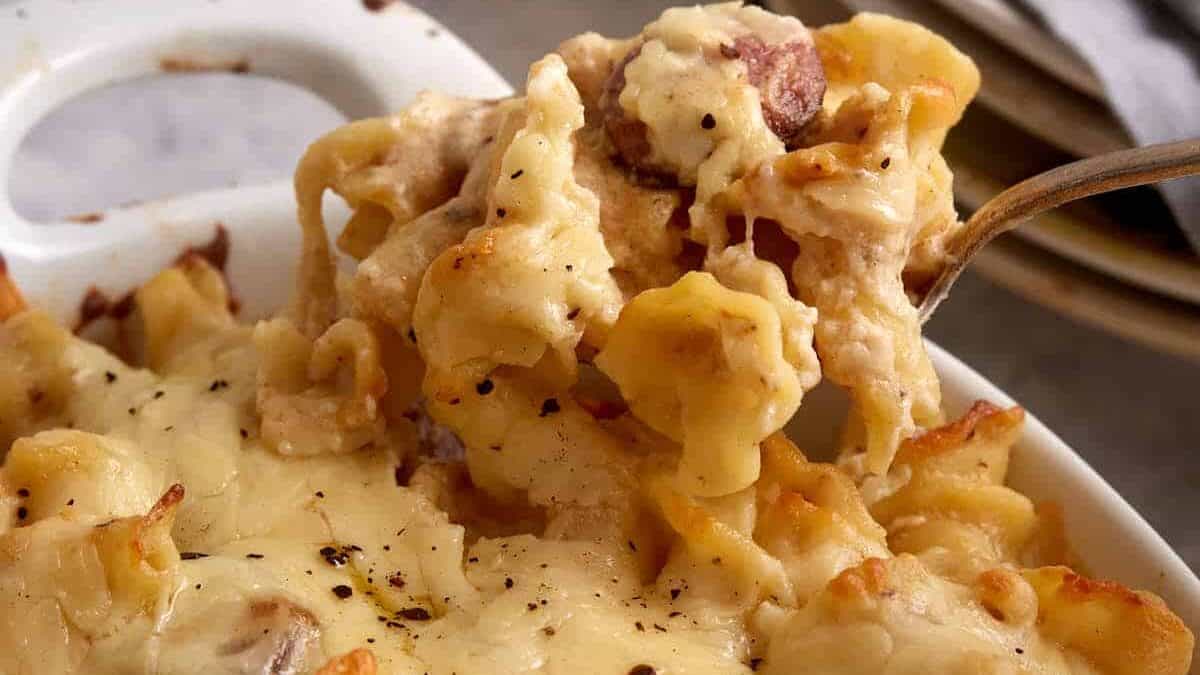 A spoonful of smoked sausage pasta being removed from a baking dish.