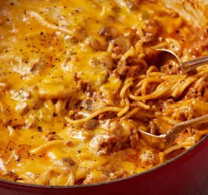 A red pot full of spaghetti casserole with two serving spoons.