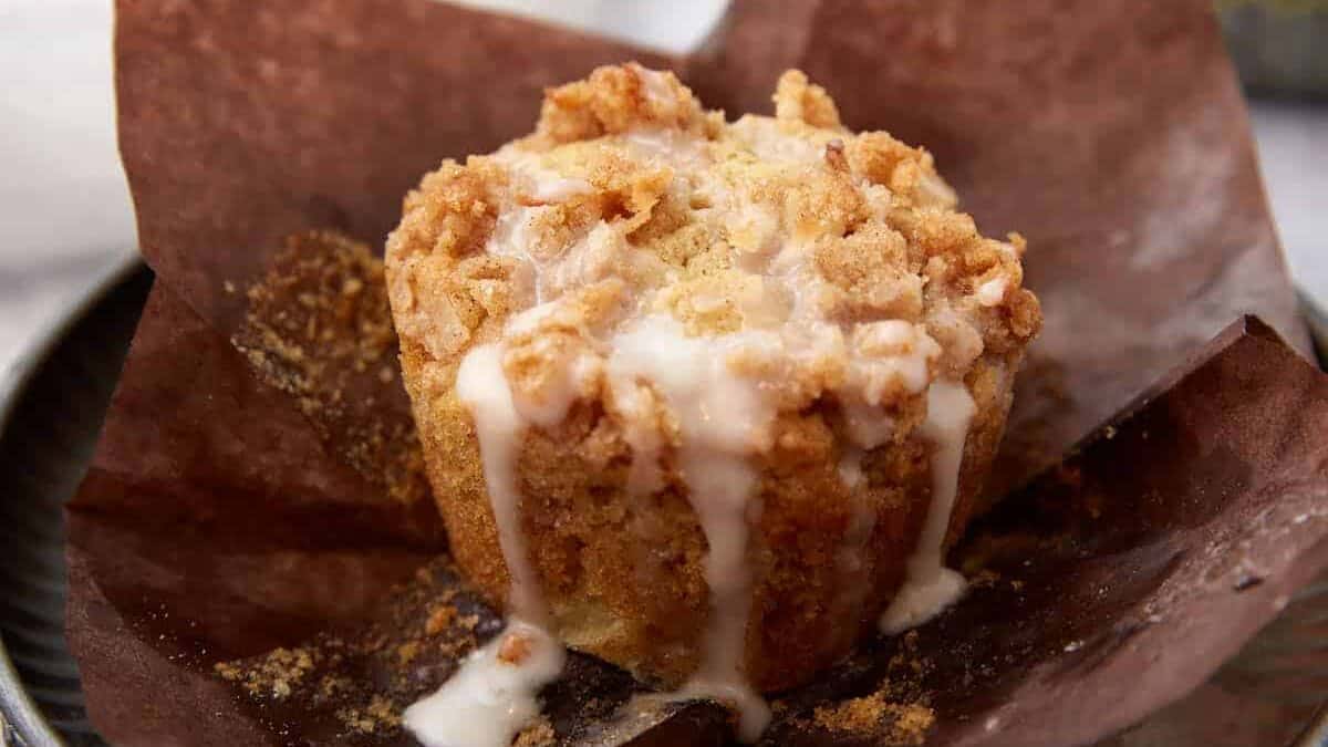 A single apple muffin with glaze dripping down the sides.