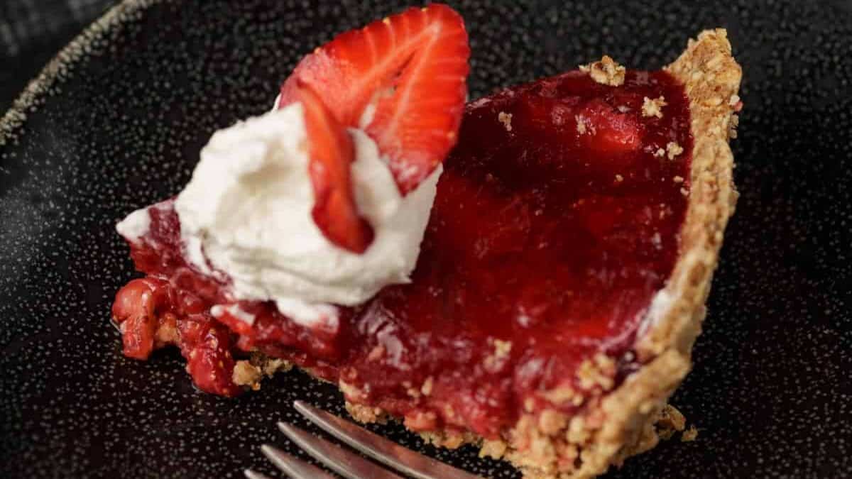 A slice of strawberry pie with whipped topping on a plate with a fork