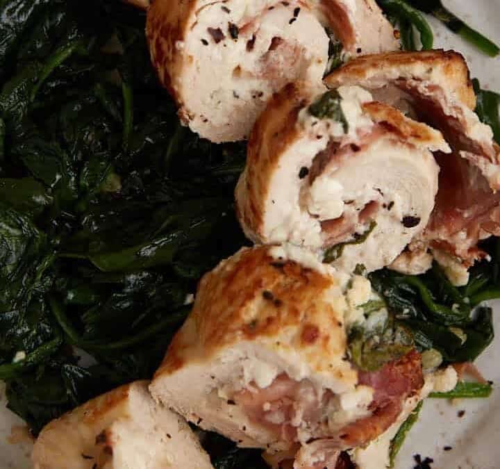 Sliced chicken breasts on a bed of spinach on a plate.
