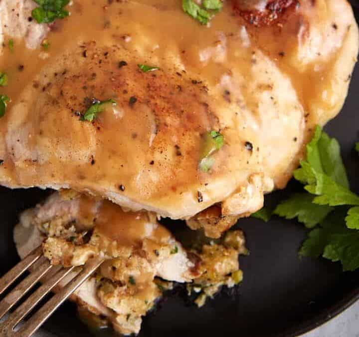 A stuffed pork chop on a plate covered in gravy.