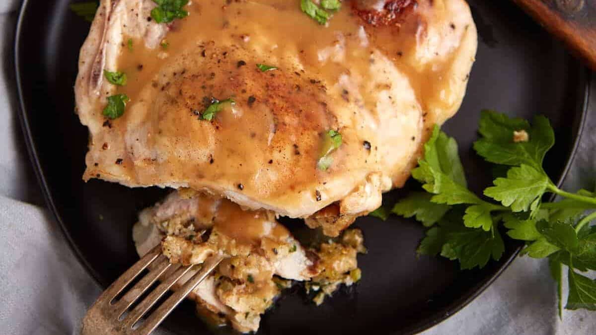 A stuffed pork chop on a plate covered in gravy.