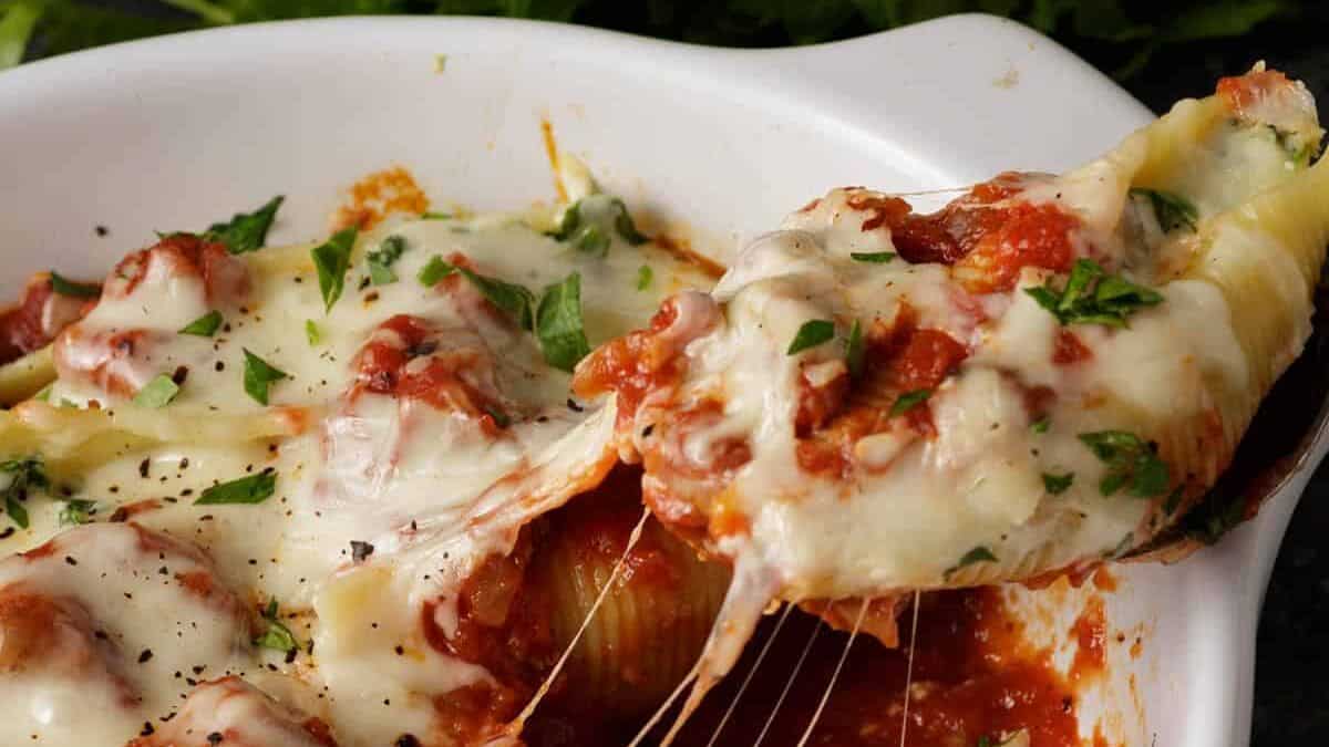 A stuffed shell being removed from a baking dish