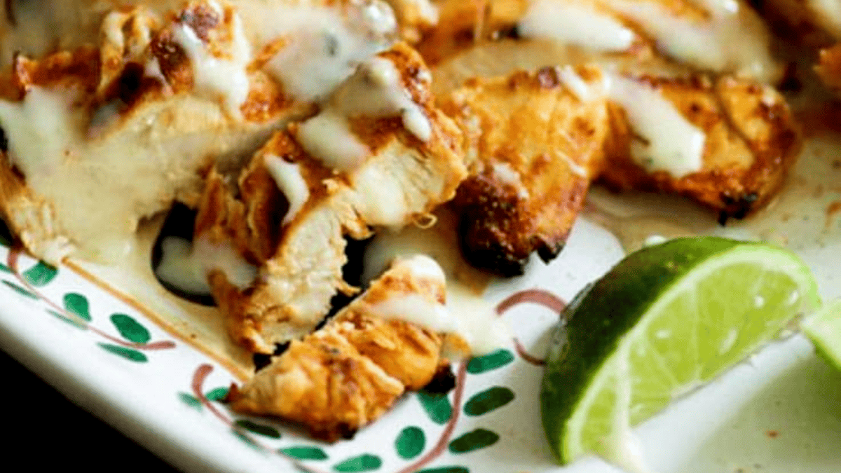 Grilled chicken breast slices topped with a creamy white sauce, served on a decorative plate with a fresh lime wedge on the side—perfect for those seeking healthy grilled dinners.