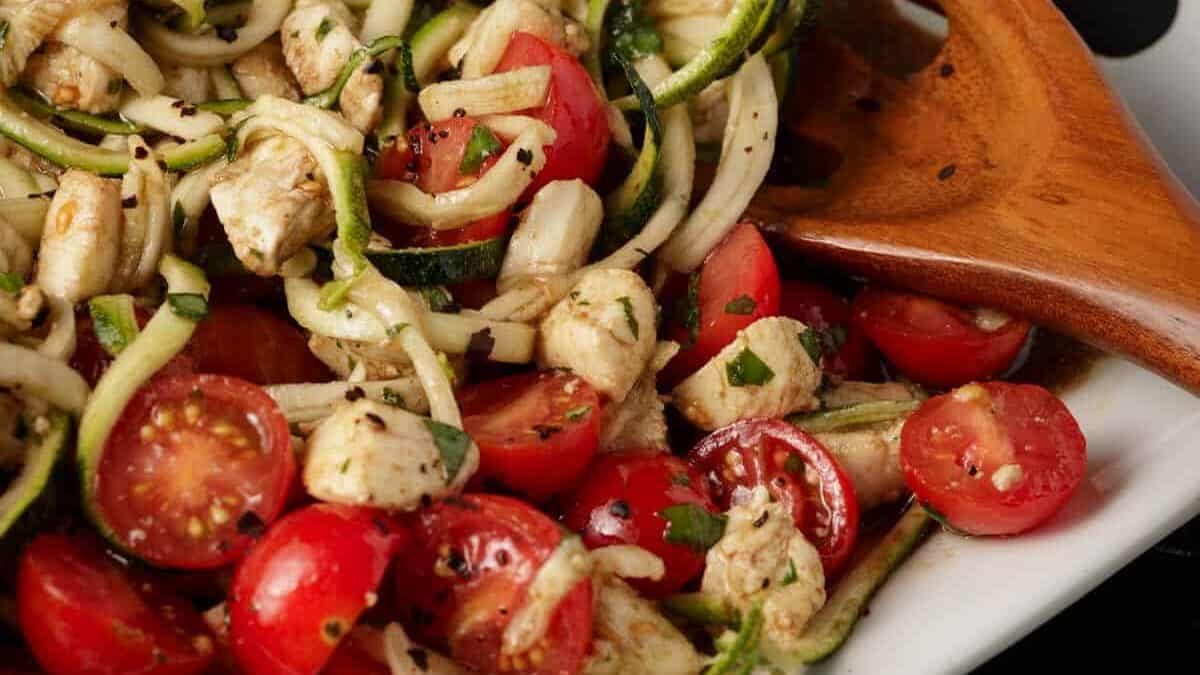 A white platter of zoodles mixed with tomatoes