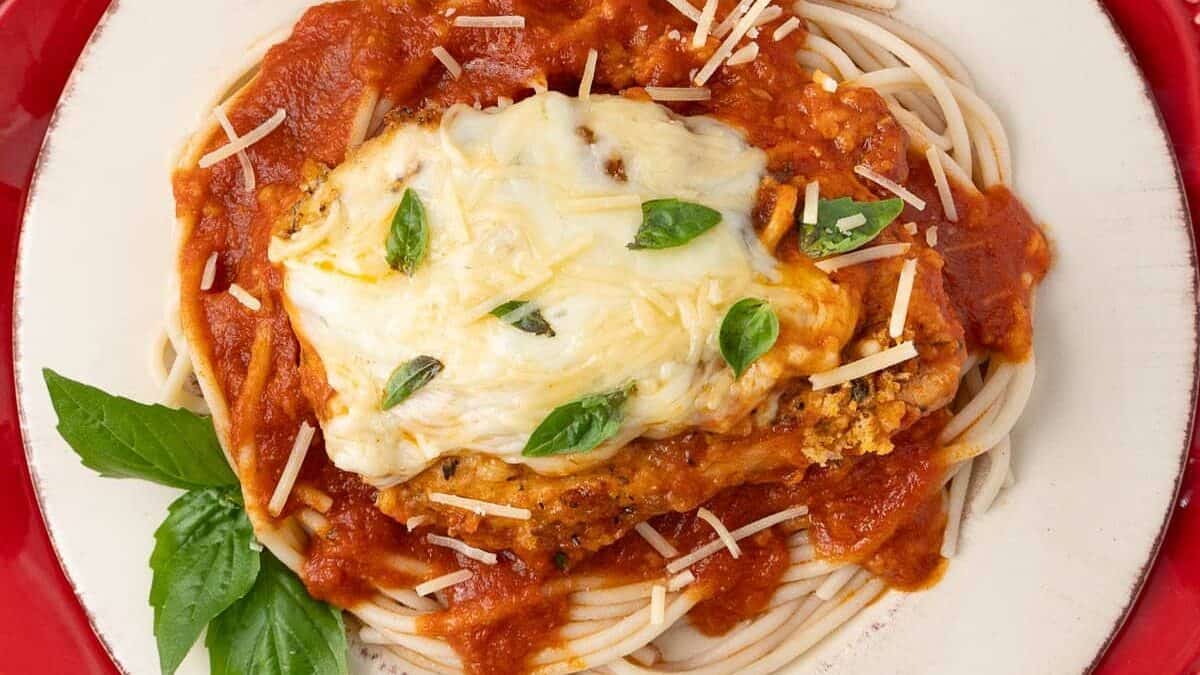 A plate of spaghetti topped with marinara sauce, a breaded chicken cutlet covered with melted cheese, garnished with fresh basil leaves and shredded Parmesan cheese—dinners so delicious you'll savor every bite.
