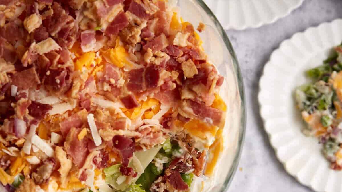 A bowl of seven layer salad next to individual servings.